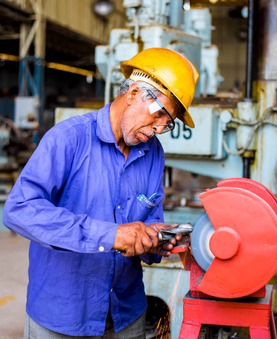 A factory worker in a hard hat and safety glasses working at a machine